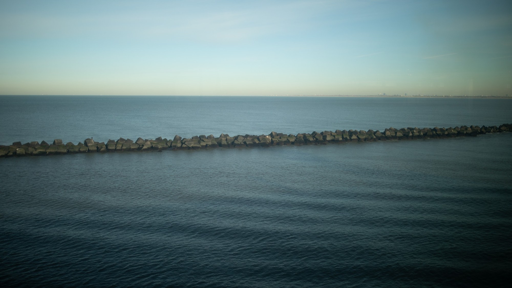 A low sea defence stretching across calm blue water