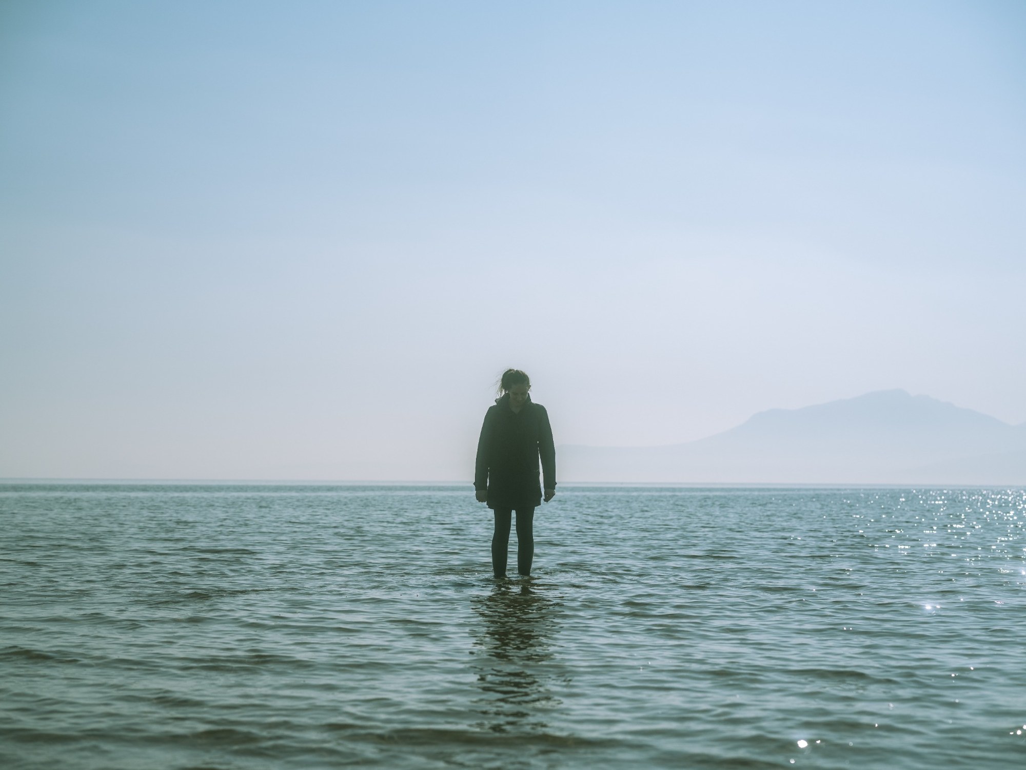 A person standing in still water, with distant hills beyond